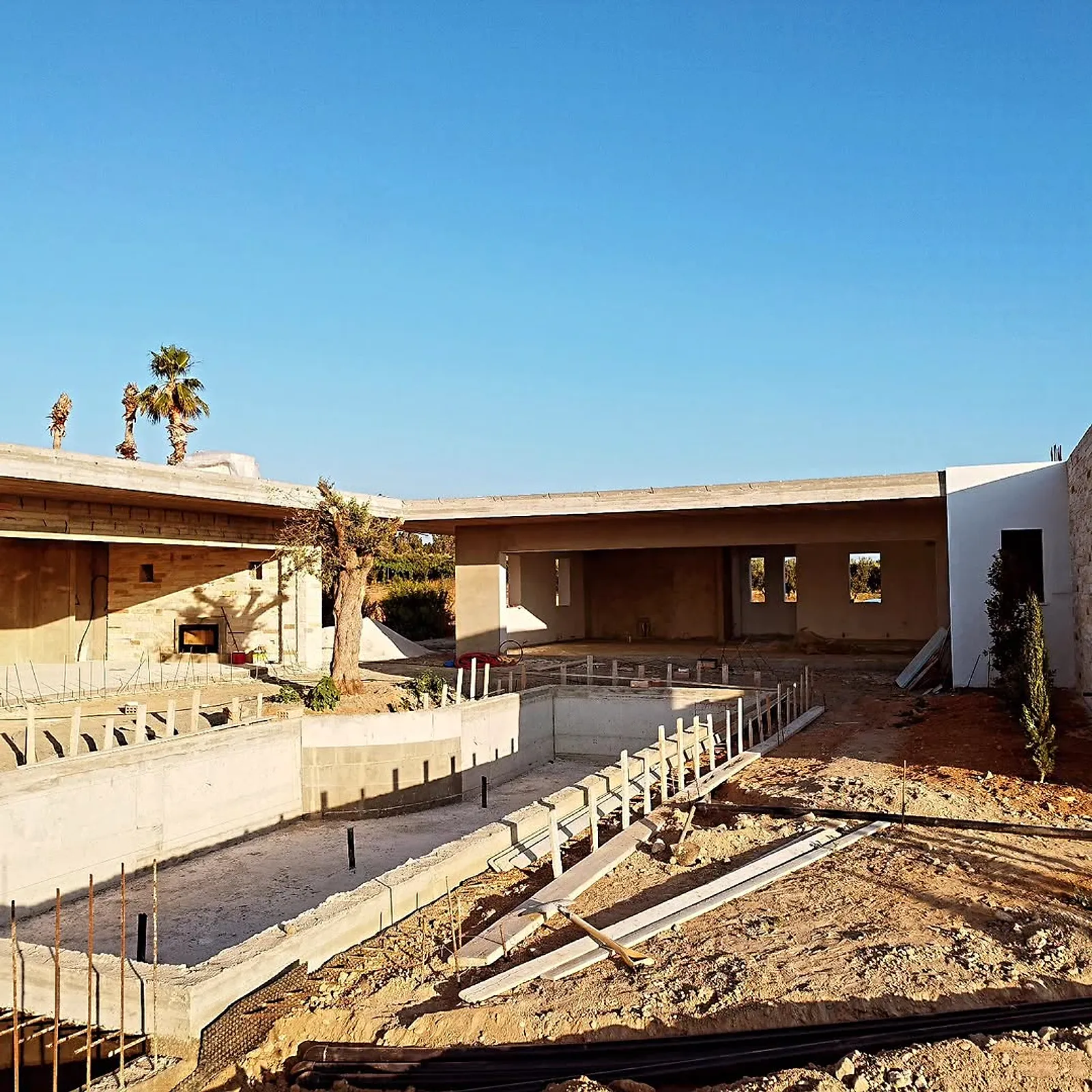 Concrete pool shell next to the stone house under construction